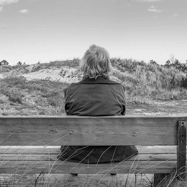 senior woman sitting on a bench overlooking the sand dunes